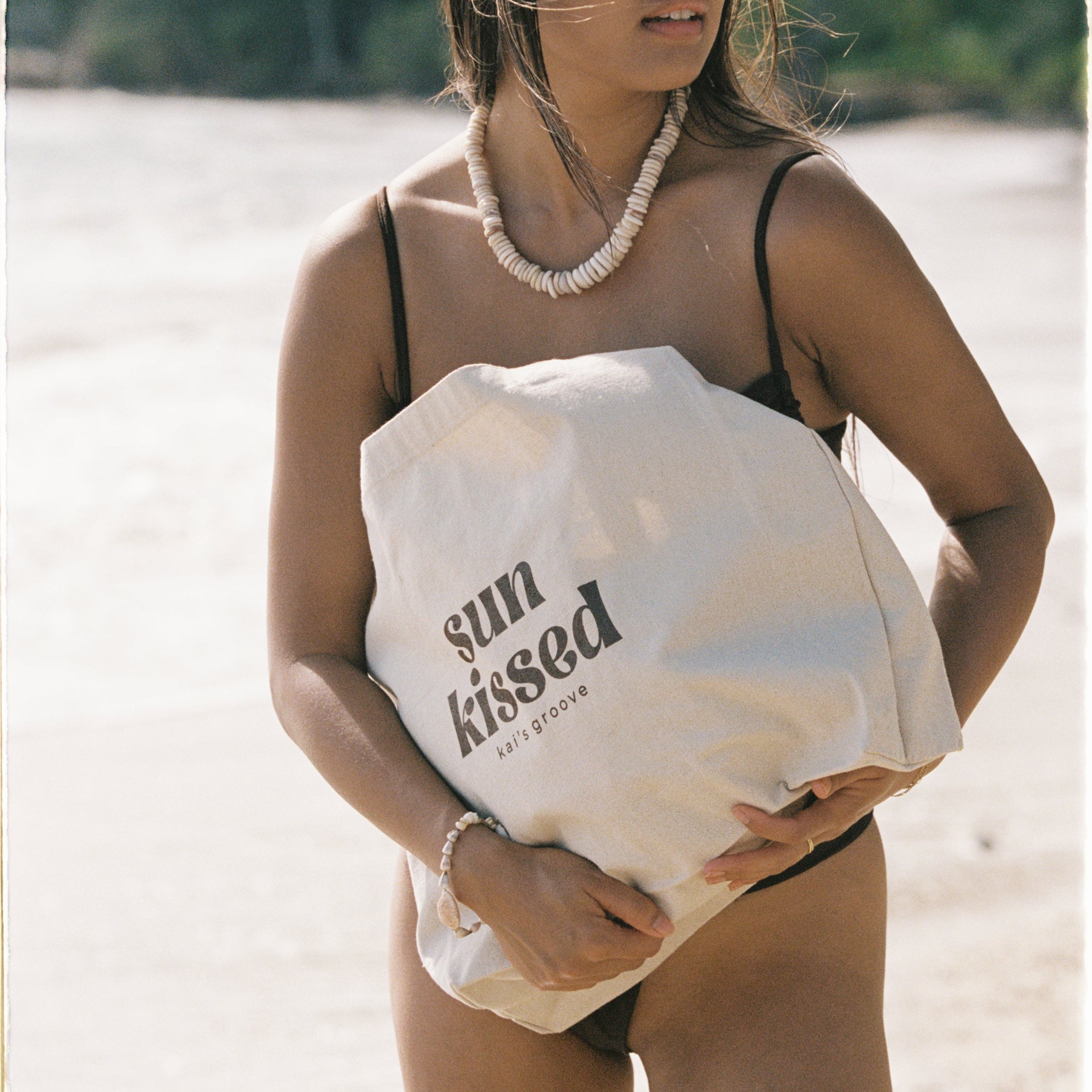 Woman holding a 'sun kissed' bag on a beach