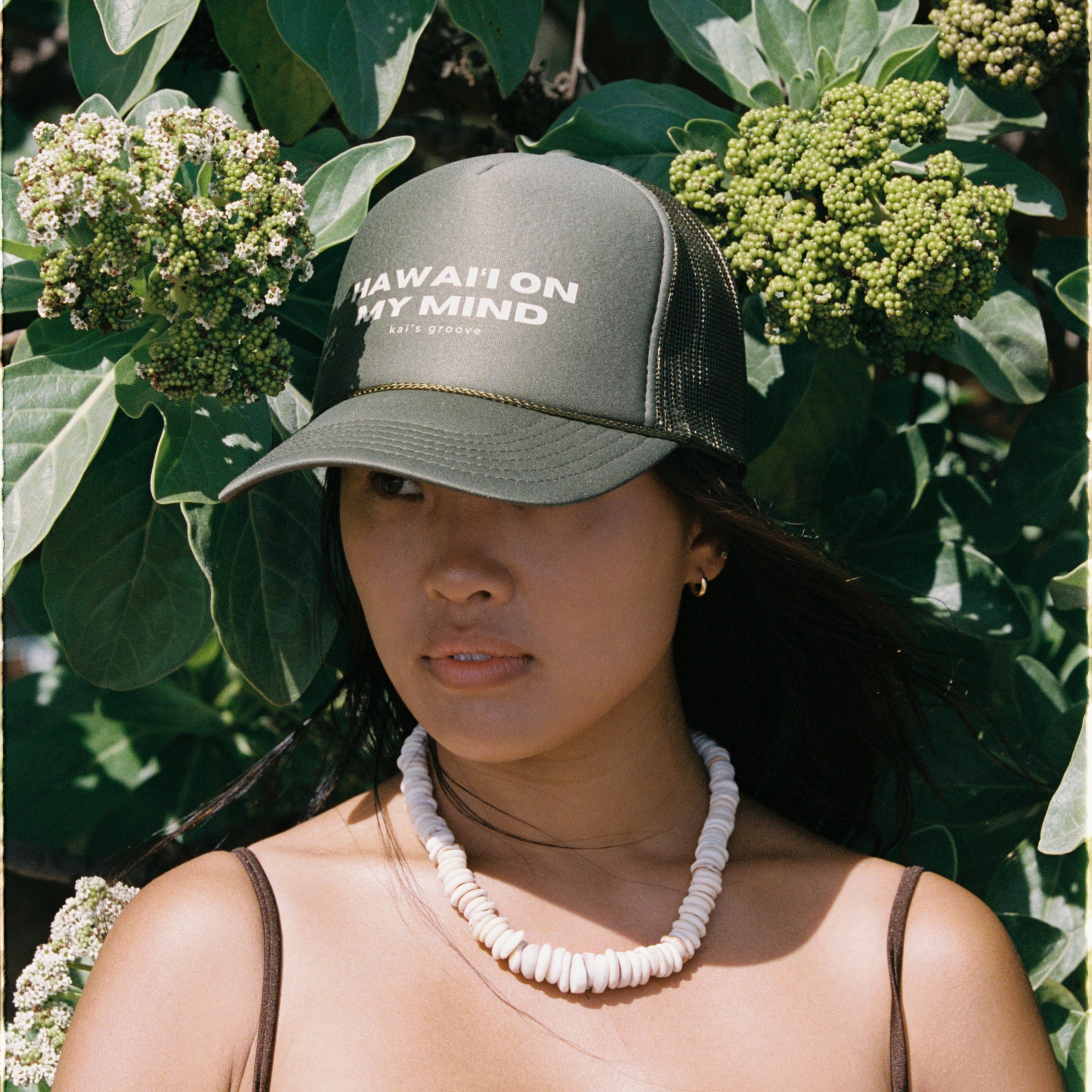 Woman wearing a cap with text "ISLAND WAHINE" in front of green foliage in Hawai'i