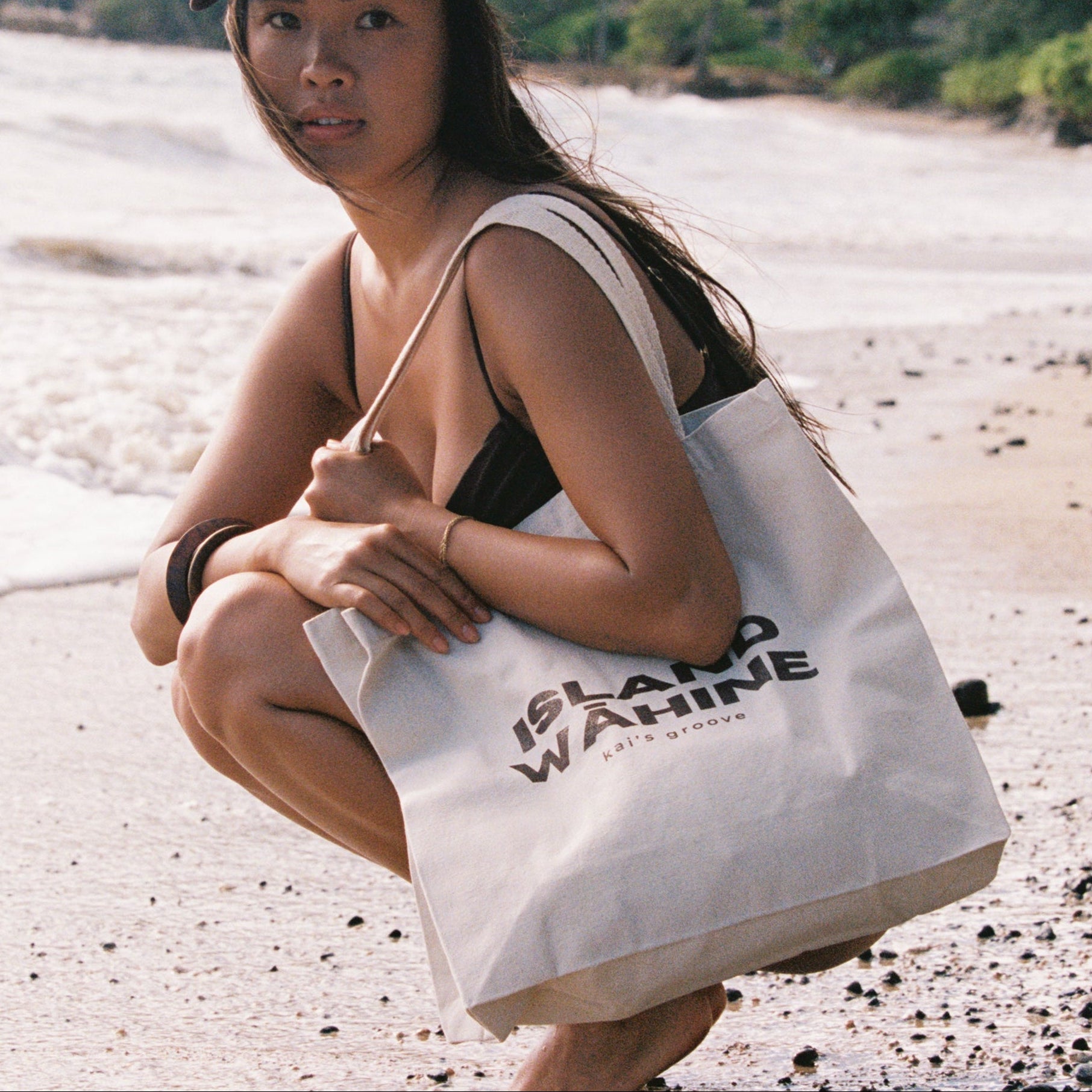 Woman on a beach holding a white tote bag with a logo island wahine