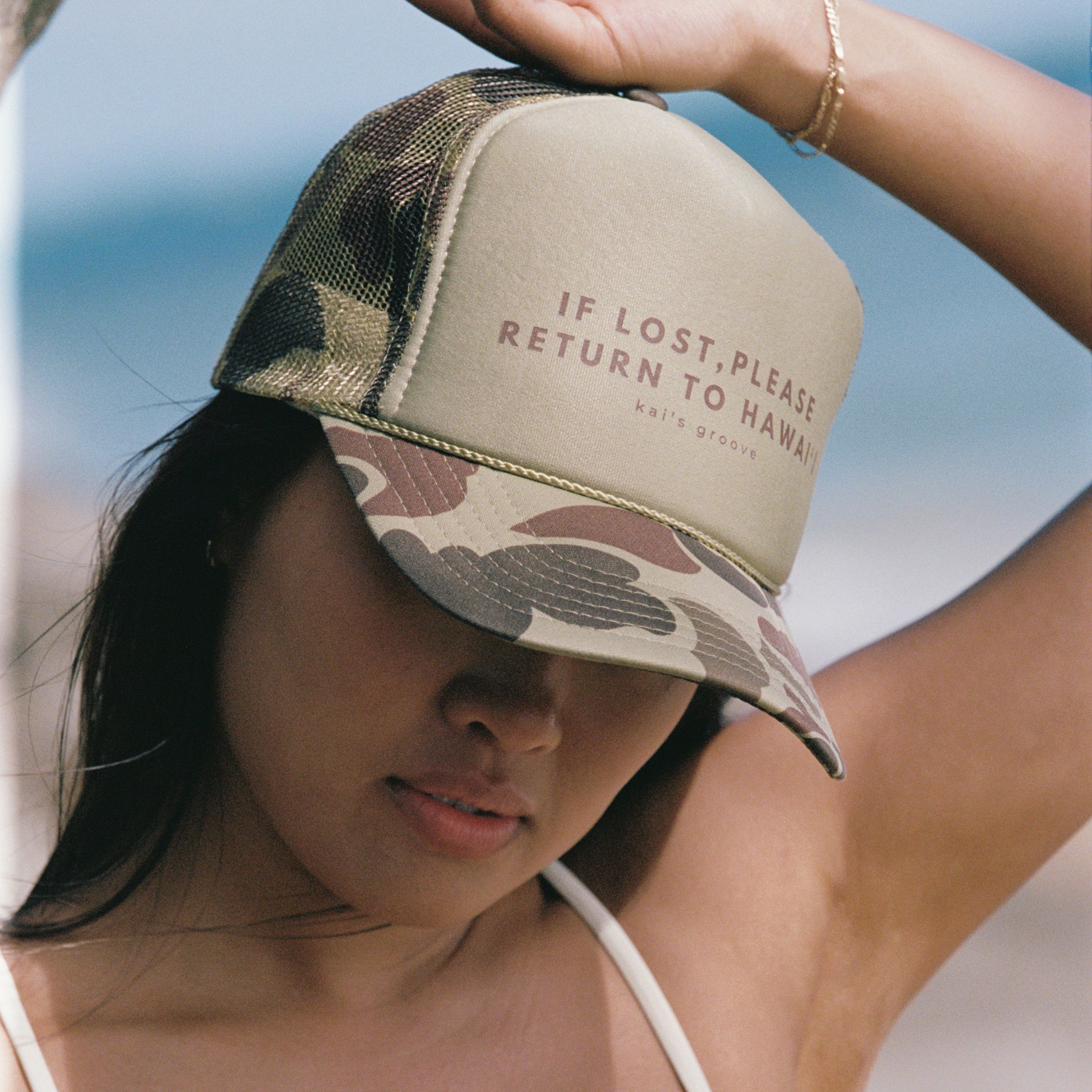 Woman wearing a cap with text, standing outdoors with a clear sky.